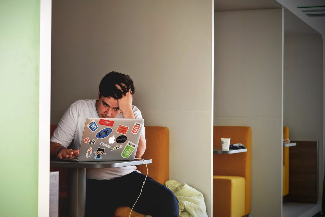 Frustrated coder using a laptop with a bunch of stickers.