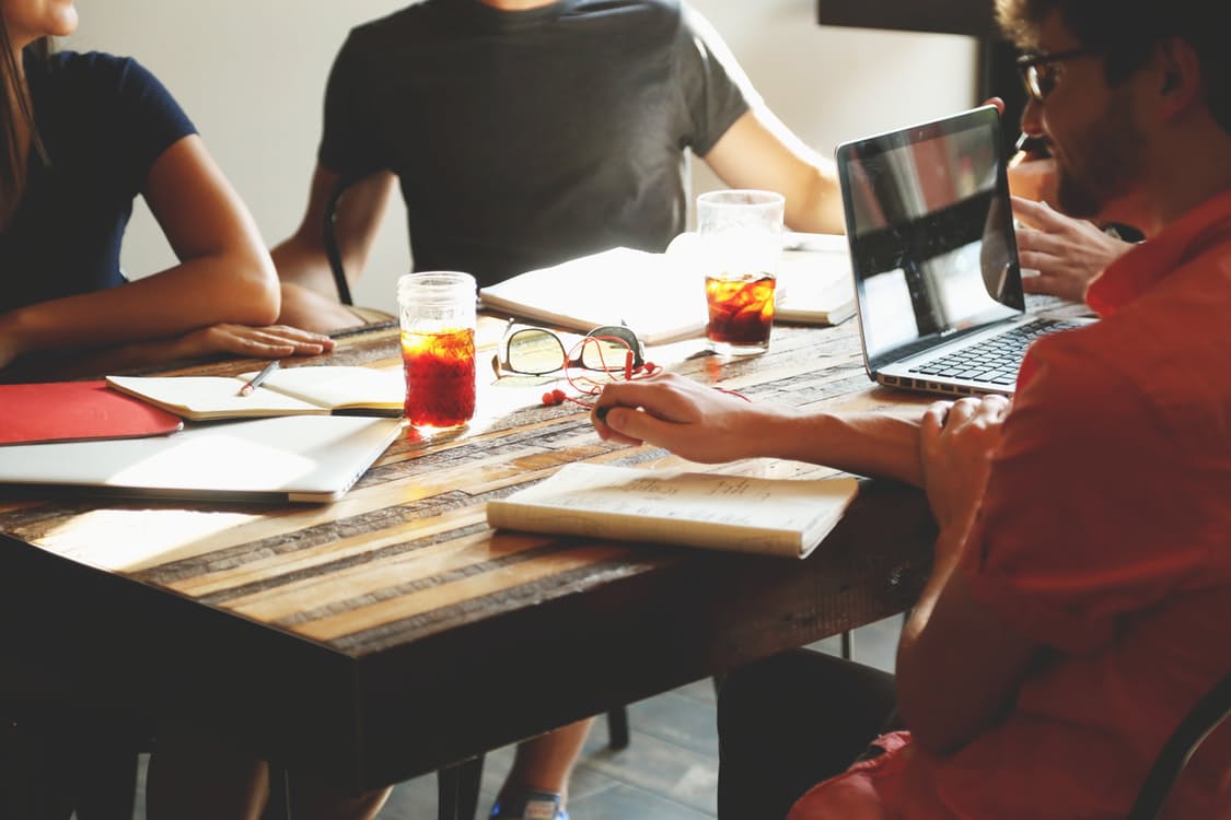 Team members meeting at a table with laptop and iced drinks.