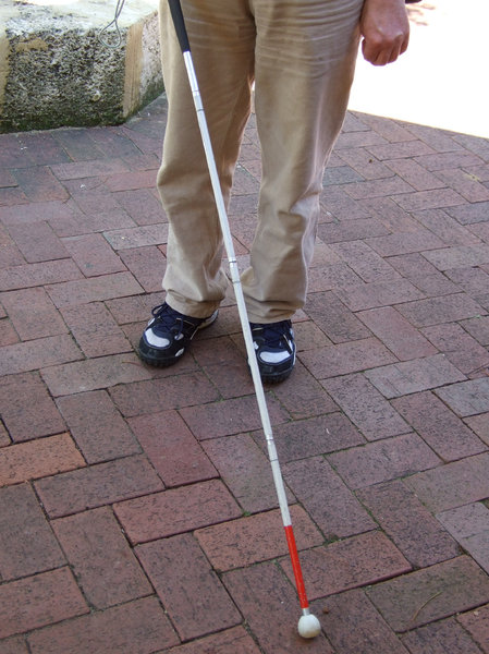 Blind man using a white cane with a red tip.